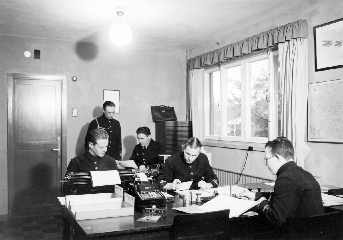 Interiör av divisionskansli, kasern I, på F 2 Roslagens flygflottilj, 1939. Fyra män i arbete vid skrivbord, en man stående.