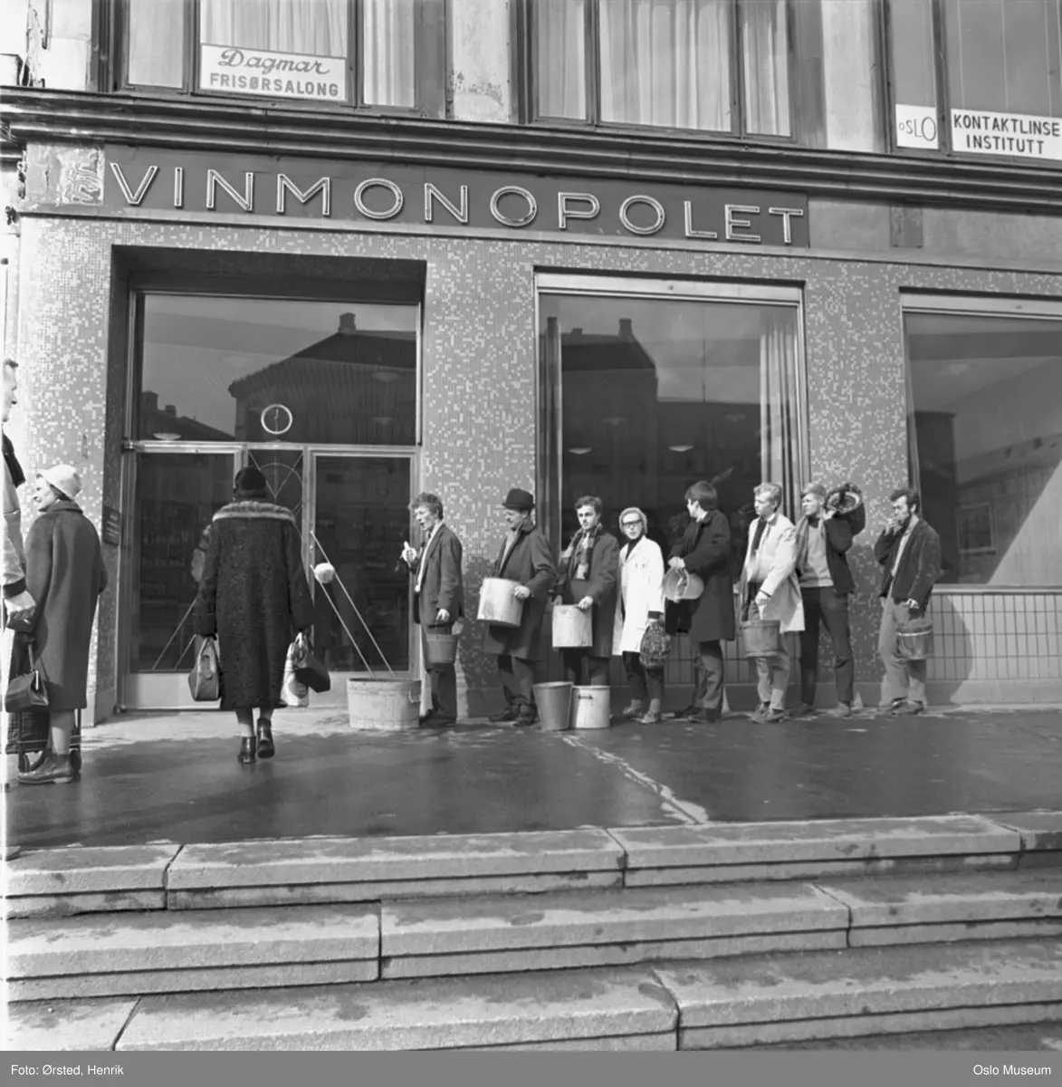 Vinmonopolutsalg, inngangsparti, kunder, kø, bøtter, vinballonger, 1. aprilspøk