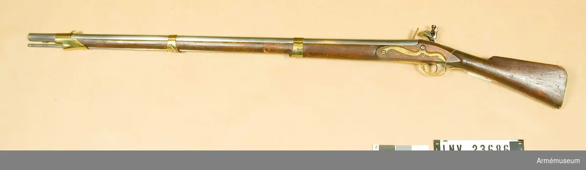 Samhörande nr är: 23686-7, gevär, bajonett.
Flintlåsgevär. Reparerad m/1805.
Grupp E II. 
Nominalkaliber 20,04 mm.  Verklig kaliber 19,85 mm.Geväret är sammansatt av delar från diverse äldre gevär.  Pipan är av 1725 års modell och filad rund.  Siktet är det ursprungliga, men med nedfilade vingar. Kornet är  av mässing, båtformigt och högt.  På pipans översida finns krönt N T (Norrtälje) T S och C G. På  vänstra sidan finns ett inslaget M och några otydliga stämplar.  På undersidan finns en otydlig stämpel och, täckt av laddstocks-  fjädern, en med bokstäverna P A. Häftena är bortfilade och pipan  är något förkortad. På pipans undersida, 4 cm bakom mynningen,  sitter en bajonettklack.Låset ser ut att vara m/1725. På bleckets utsida finns en stämpel med bokstaven B eller möjligen med ett monogram av I B.Stocken är mörkbrun, av björk och m/1805. På kolvens vänstra sida är bokstäverna T S och numret 35 inslagna.Sidblecket är taget från ett gevär m/1747. Det har på utsidan en stämpel med I P M och dessutom är där inslaget numret 179. På insidan sitter en stämpel med A S B. Övriga beslag är de vanliga m/1805. Bakplåten har en rätt lång, över kolvryggen utskjutande flik samt fasthålles genom en mindre skruv, som går genom denna flik, och genom två större, med stora stöthuvud försedda skruvar. På flikens översida sitter en otydlig kronstämpel och på bakplåtens insida finns bokstaven G. På varbygelns insida sitter en stämpel med S V. Nedre bandet har på undersidan en framåtriktad, avrundad spets. Mellanbandet är både fram och bak över laddstocksrännan litet utdraget. Näsbandet har kraftig, över laddstocksrännan gående kappa. Detta band och nedre bandet fasthålles av stift, mellanbandet av övre rembygelns skruv. Den nedre rembygelns skruv går genom varbygeln strax under dess främre ände.Laddstocken är cylindrisk. I ena änden har den gängor för kratsen. I samma ände är huvudet genombrutet av en 3 cm lång springa.I Modellsalens reversal återfinnes geväret som "Mousquetter och Infanteri Gevär. Svenska. Med flintlås. 1805 års reparationsmodell" och bajonetten under, "Bajonetter Infanterigevärs, Svenska, 1805 års reparationsmodell". Jfr AM 1932:4190