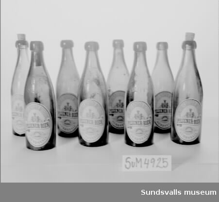 Tretton pilsnerflaskor från Sundsvalls bryggeri aktiebolag. Flaskorna har något varierande utformning och två typer av etiketter i vitt, rött och blått. Fem av flaskorna bär texten 'SUNDSVALLS BRYGGERI AKTIEBOLAG, PILSENER-BIER, SUNDSVALLS PILSENER, SUNDSVALL'. De är också dekorerade med tryckt motiv föreställande bl.a. Sundsvalls stadsvapen. De andra tre flaskorna har etiketter med texten 'KLASS 2, SUNDSVALLS BRYGGERI AKTIEBOLAG, PILSNER, INNEHÅLLER SACKARIN, SUNDSVALLS PILSNER, SUNDSVALL'. Samtliga etiketter är tillverkade hos Lithografiska AB i Norrköping.