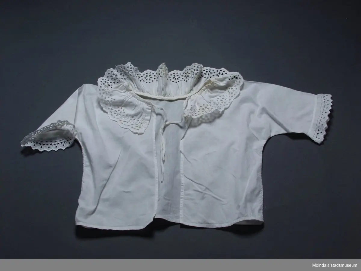 Vit spädbarnsskjorta i bomull med brodyr runt halsringning och ärmar.