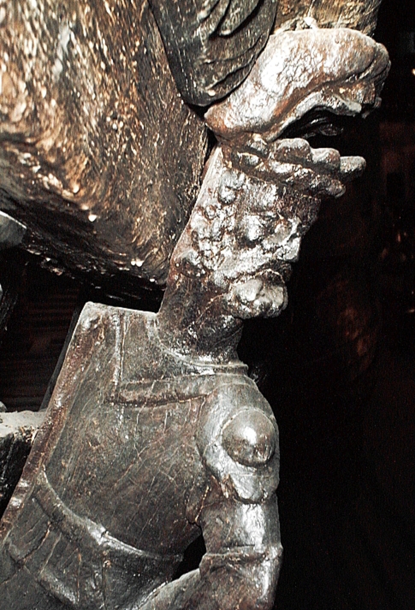 Skulptur föreställande en mansfigur iförd romersk rustning. På huvudet har figuren en taggig krona med bred "stenbesatt" kronring. Bakom huvudet syns ett stort snäckskal. Ansiktet pryds av ett stort, relativt kortklippt och krusigt skägg. Figuren är iförd en långärmad rustning med stålharnesk, axelskydd och knäskydd. Rustningen är, som typ betraktad, ett mellanting mellan romersk rustning och renässansrustning.



Figuren står vinkelrätt mot bakstycket, med höger sida tryckt mot bakstycket och vänder följaktligen den vänstra sidan utåt. Kejsaren har huvudet vridet kraftigt åt vänster så att han blickar mot betraktaren när denne står framför skulpturen. Den vänstra handen vilar mot höften. Höger arm, som saknas, har troligtvis hållits bakåt, bakom ryggen. Figuren vilar på höger ben, medan vänster ben hålls böjt. Möjligen avser framställningen att återge kejsaren i rörelse framåt, med tanke på att kroppen är framställd i profil och inte en face. Figuren står på en sockel, vilken pryds av en grinande maskaron samt en namninskription.



Upptill är bakstycket framdraget i en enkel "huvudplatta", med en delvis kvartscirkelformad profil. Skulpturens baksida uppvisar tre snedställda, olika djupt liggande fält. De tre fälten, som utgör anliggningsytor, ger skulpturen en trappstegsformad profil.

Sockeln är skadad nedtill och namninskriptionen går ej att tyda. Figurens högra arm saknas. I övrigt är skulpturen välbevarad.



Text in English: A sculpture representing a male figure wearing a Roman armour. On the head there is what looks like a flat crown and on the board behind the head there is possibly a large sea shell. The face has a large curly and mostly clipped beard and is framed by curly hair. The figure wears long-armed armour with a steel curass, shoulder guards and knee guards of a type reminiscent of both Roman and renaissance amour.



The figure stands at a right angle to the back-board of the sculpture, with its right side pressed to the back-board and the left side outermost. The figure''s head is turned to the left lookimg over his shoulder. The left hand rests on the hip were there originally would have been a sword. The right arm, which is missing, was held behind the back of the figure. The body rests on the right leg, the left leg is bent, the pose is possibly meant to show the figure moving forward. The figure stands on a plinth decorated with a mask and a name inscription.



The upper part of the back extends obliquely upwards in a simple"head board".



The back has three obliquely placed surfaces of different depths, that are areas of attachment. The surfaces make the sculpture looks like a step-ladder in profile.

The plinth is damaged and no letters on the inscription is visible. The figure''s right arm is missing. Otherwise, the sculpture is well preserved.