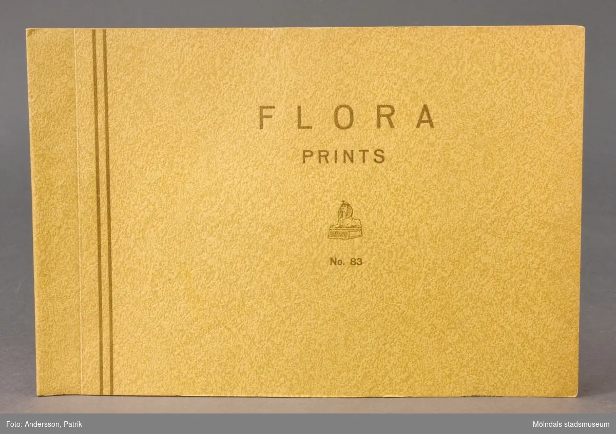 Häfte med prover "Flora Prints No. 83". Pärm av gult mönsterpressat grovt papper med brunt tryck. Papyrus logotyp med sfinx. Produktinformation på engelska; M.G. Sulphite Paper. Provark i olika storlekar, ordnade lättöverskådligt och märkta med siffra. Pappersprover av enfärgat, polykromt, blommönstrat, randigt samt julpapper. Litteratur: Papyrus 1895-1945, Minnesskrift, Esseltes Göteborgsindustrier AB, Göteborg 1945.