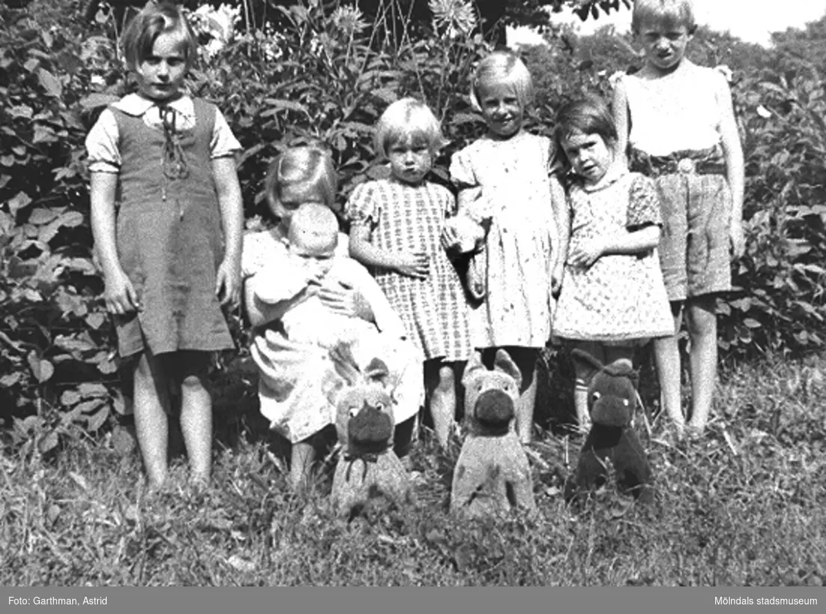 Barn boende vid Kvarnfallet 31, 1930. De står på en grässluttning framför några träd. Det är bland annat givarens mostrar och fastrar samt grannar till dem.