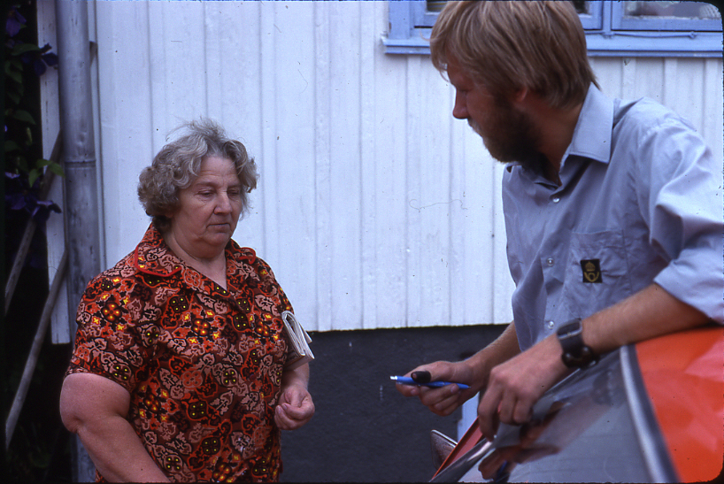 Lantbrevbäraren Mikael Mattsson besöker Maj-Britt Wessberg i Räfsta i Vallentuna. De står utanför huset, hon har en tidning under armen och han lutar sig mot bilen, med en penna i handen. 