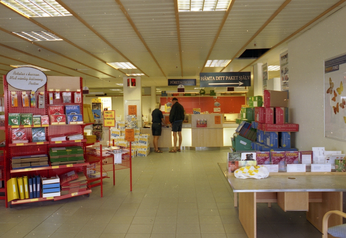 Interiör från allmänhetens avdelning på regionpostkontoret Kungshörnet i Uppsala, 1996. I kassahallen finns bland annat paket, kuvert och brevpåsar till försäljning. Postkontoret är utrustat med ett kösystem och en självservice för paketutlämning.