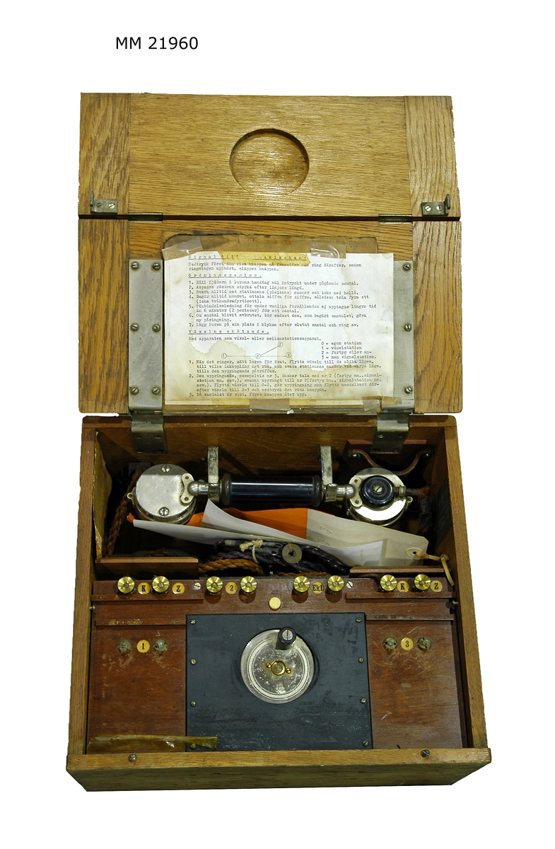 Lådtelefon med inbyggd växel för tre anslutningar. Användningsinstruktion i locket, samt två fotografier.
X 619.