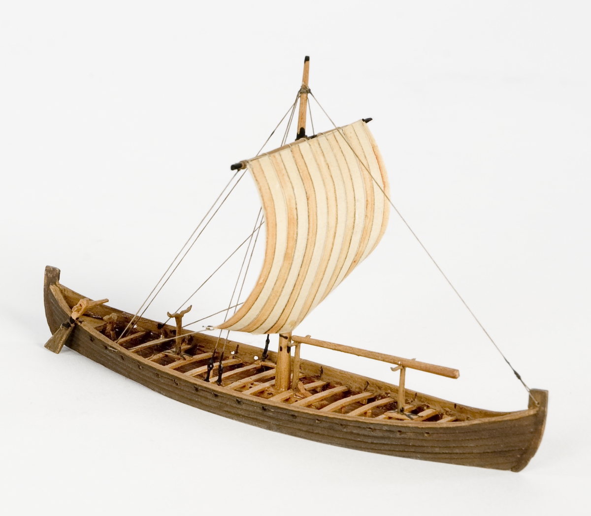 Fartygsmodell av trä. Vikingaskepp på vattenlinje. Sexton roddbänkar, styråra på styrbords sida. Riggad med en mast och ett röd-och vitrandigt segel av papper. Tältspira upplagd på bockar för om masten. Mörkbrun färg.
Skala 1:200Föremålets form: Vattenlinjemodell