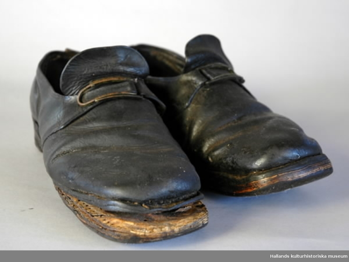 Ett par skor av läder, med spännen. Mycket slitna. Längd 28 cm. Tåbredd 9.5 cm. Hälbredd 6.3 cm