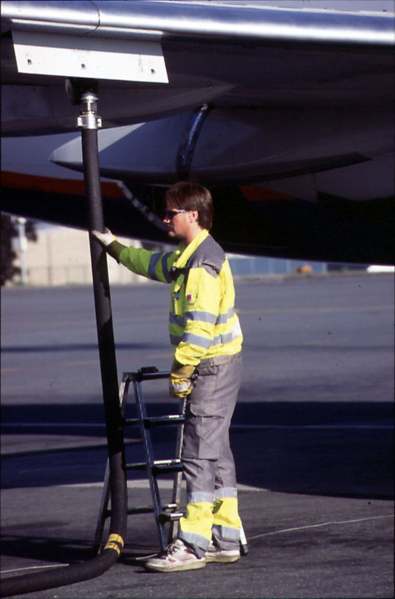 Lufthavn, 1 person, bakkepersonell, fyller drivstoff i vingen på 1 fly.