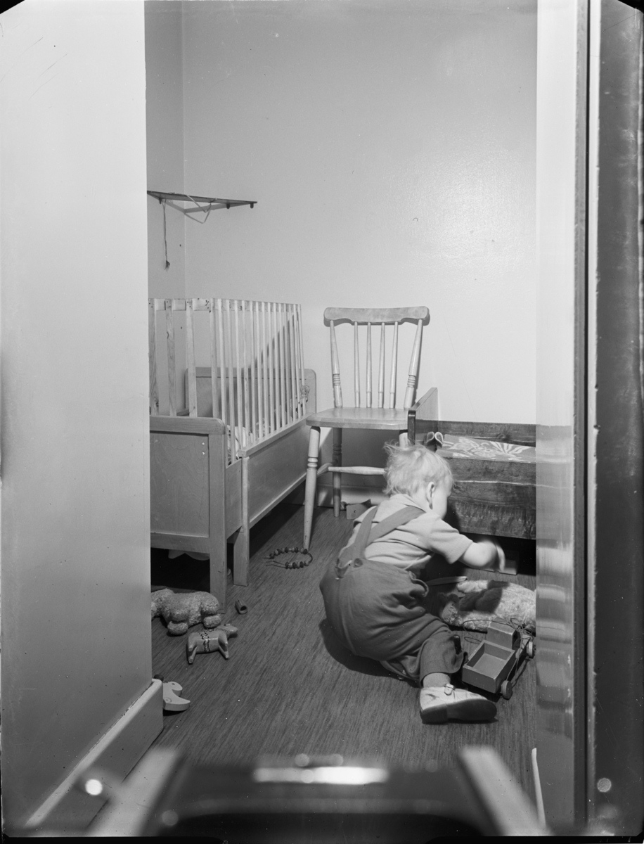 "Husmor med barn i hemmiljö" 
Sovrum med barn som leker
Barnsäng med sekundär anordning av spjälor
Interiör