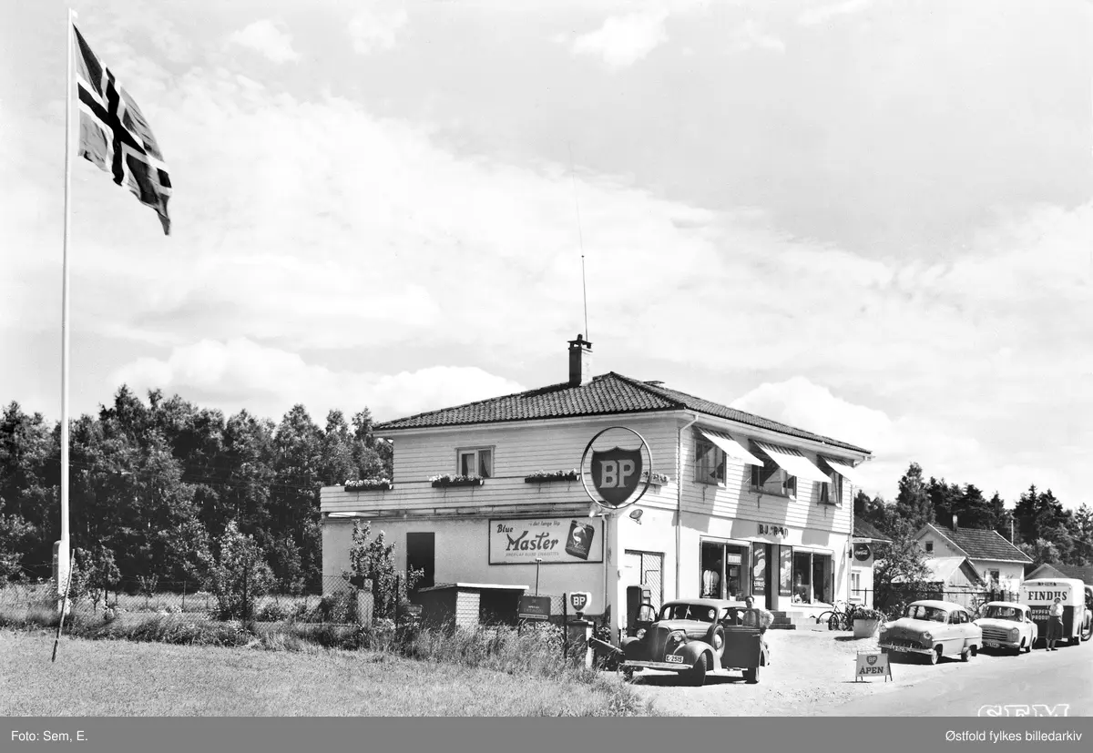 Bjarne Røds kolonialforretning, Ingedal i Skjeberg ca. 1953-1959. Postkort.
BP-stasjon, Findus, fiskebil?
Bil nummer to kan være Opel Rekord som kom først i 1853.
Reklameskilt for Blue Master, tobakk.