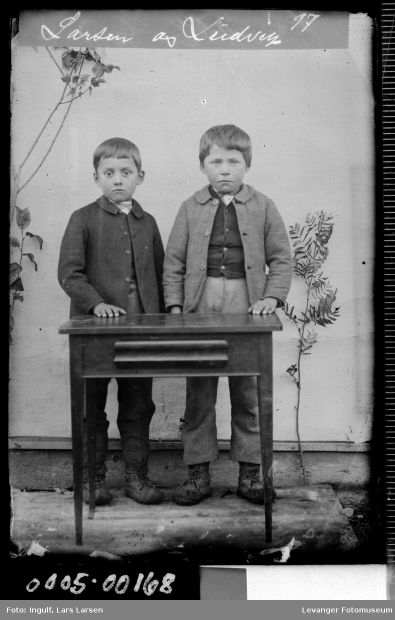 Portrett av to gutter ved et bord i helfigur.