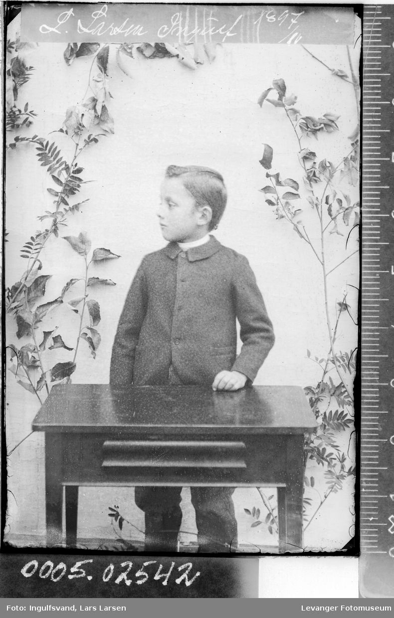 Portrett av en gutt som står bak et bord.