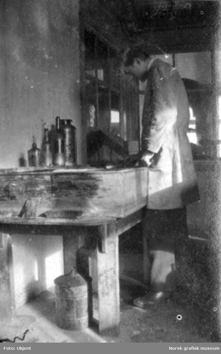 En mann i frakk står ved et arbeidsbord på Dreyers Reproduktionsanstalt.

Albumtekst:
"Brandstifteren i funktion (han er blit forsigtig nu)"