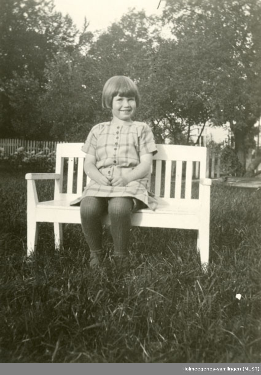 En jente sittende på en liten hagebenk, ant. på Holmeegenes i Stavanger.
