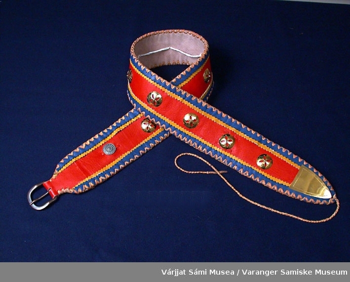 Belte av sisti (reinskinn) med sølvknapper. Beltet har rød bunn pyntet med blått og gult skinn.