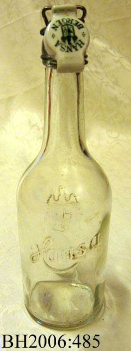 Ølflaske av klart glass med porselenskork med lukkeanordning av metall.