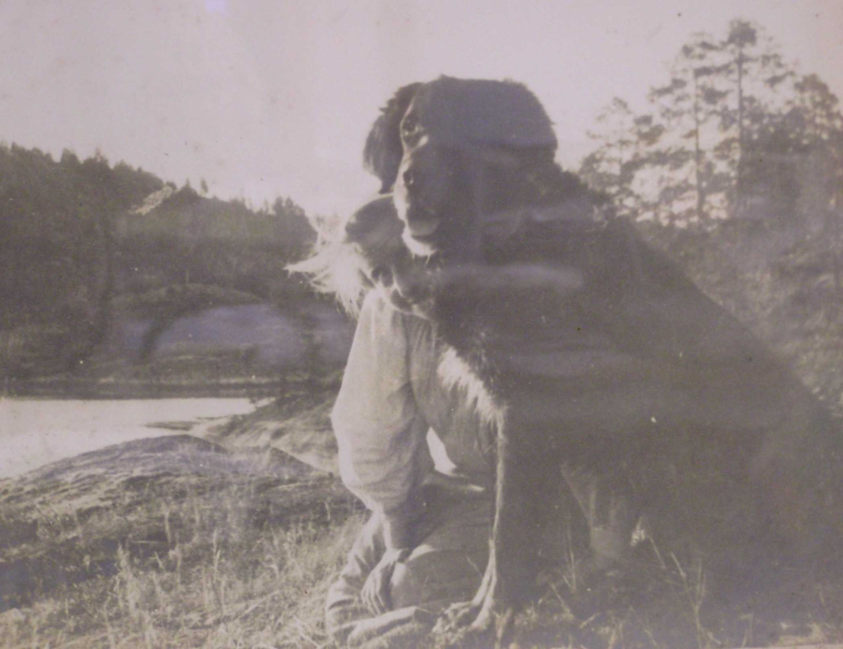 Homann, Henriette Marie  (Jeia) med hund. Jeia titter fram bak hunden, ser fjell og sjø i bakgrunn