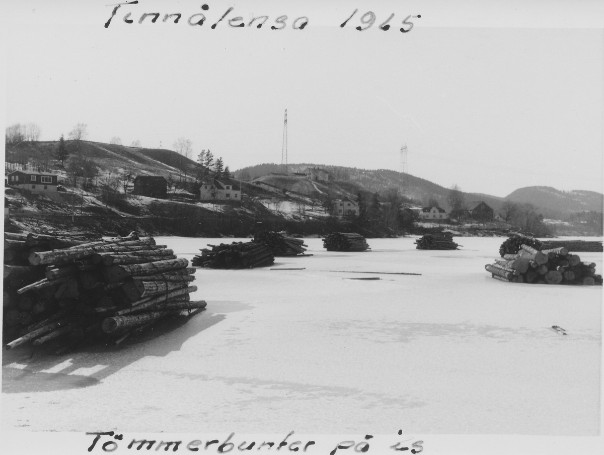 Feil info skrevet på bildet: Tinnålensa, Heddalsvannet, 1965. Tømmerbunter på is. 

Bildet viser faktisk tømmerklubber innerst i Fjærekilen. Husene ligger langs Ulefossveien. Gården som ligger oppå haugen mellom høyspentmastene er Klovholt.