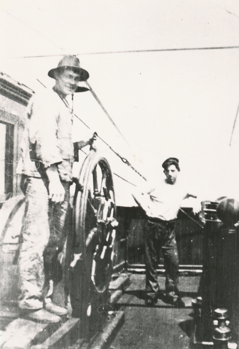 To menn står ved skipsrattet på en båt.