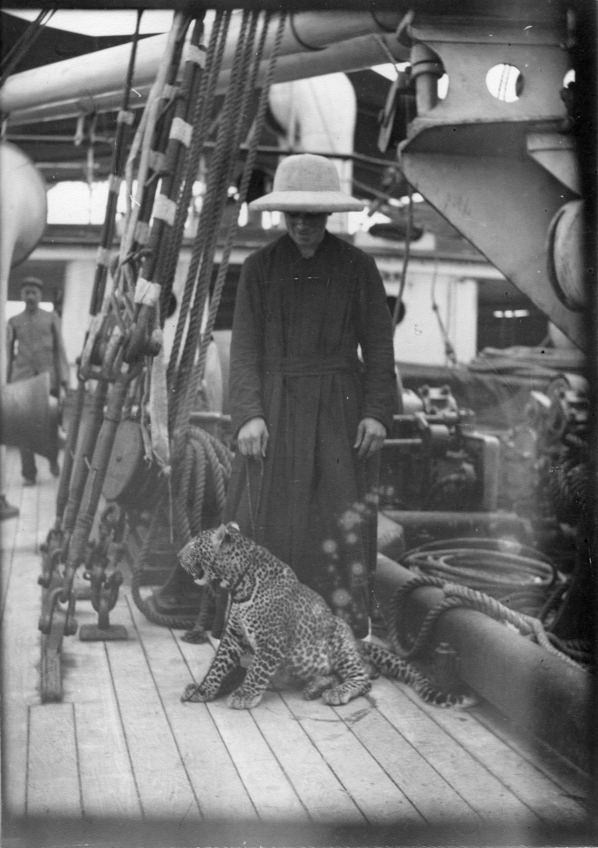 'Diverse fotografier från bl.a. dåvarande Nordrhodesia, nu Zambia, tagna av Konsul Magnus Leijer. ::  :: En man stående på däck på ett fartyg. Vid hans fötter sitter en leopard, vars koppel mannen håller i.'