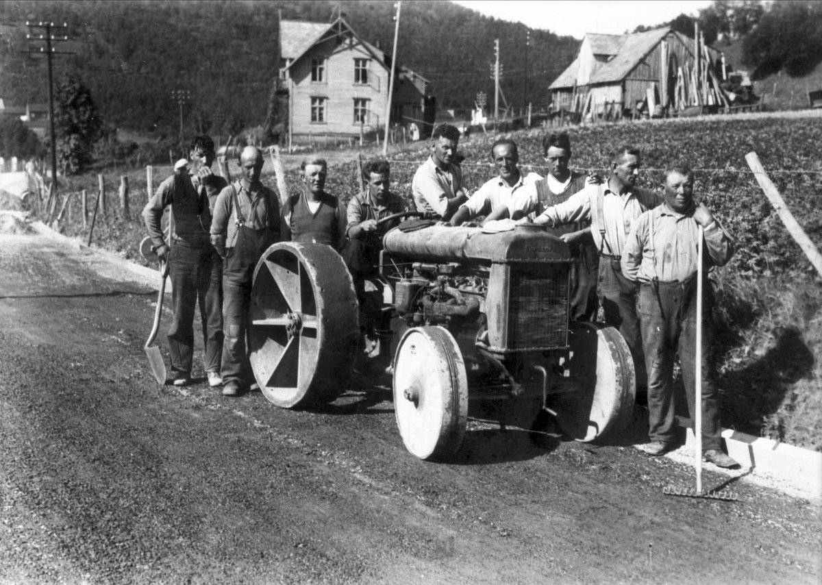 Veiarbeidere oppstilt rundt kommunens første traktor. Hus på Sama.