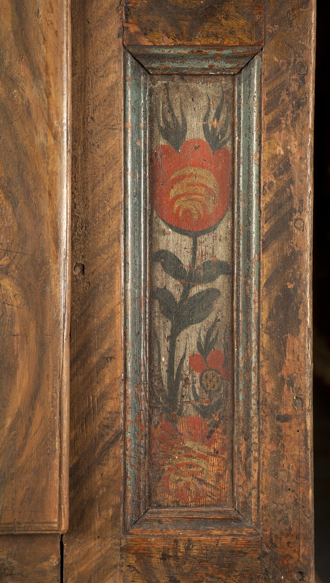 Bemålat skåp av trä, rak form. Fronten ådringsmålad i bruna nyanser. Dörr med gångjärn, beslag, lås och nyckel i järn (UM31019b). Övre delen av dörren har vit text: Ao 1790 JES, resterande initialer är oläsliga. Dörrspegel och totalt fyra sidospeglar dekorerade med stiliserade tulpaner (flammande tulpaner) i grönt, rött och gult mot vit botten. Det nytillverkade krönet är ådringsmålat i bruna nyanser, profileringar målade i två gråblå nyanser, en målad med rödaktig färg. Skåpets sidor och krönets ovansida har även de ådringsmålats med färg i bruna nyanser. Den nytillverkade lösa benställningen med hylla är ådringsmålad i bruna nyanser, de spiralvridna benen är svartmålade, liksom kulfötterna. Inredning: tre hyllor.
Benställningens mått: höjd 54 cm, bredd 110 cm, djup 53,5 cm.
Den ursprungliga målningen är sliten, framför allt på dörrens högra hörn.