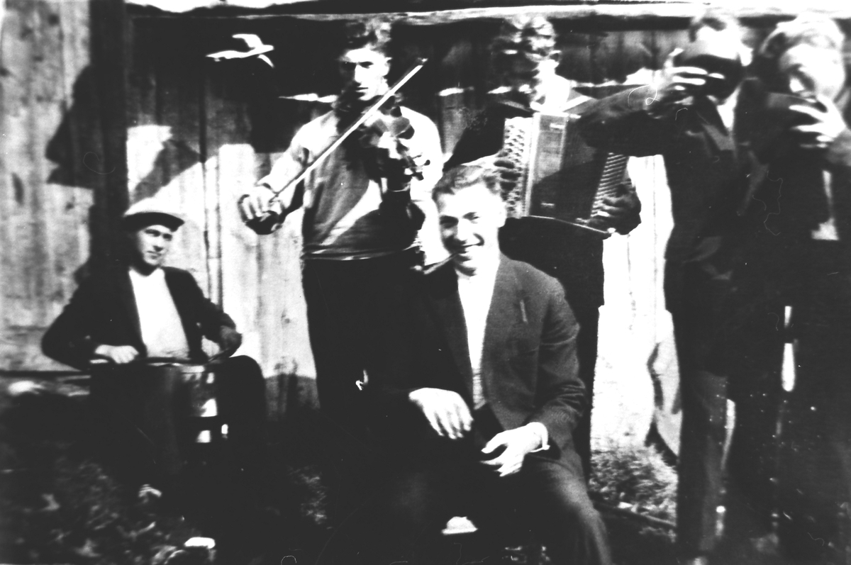 Motiv av seks menn, et spelemannslag og to herrer som drikker av en skål. Avslutning av slåttedugnad på Skotet ca.1928-30.