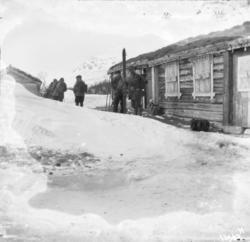 En gruppe menn står foran en laftet tømmerhytte eller seterh