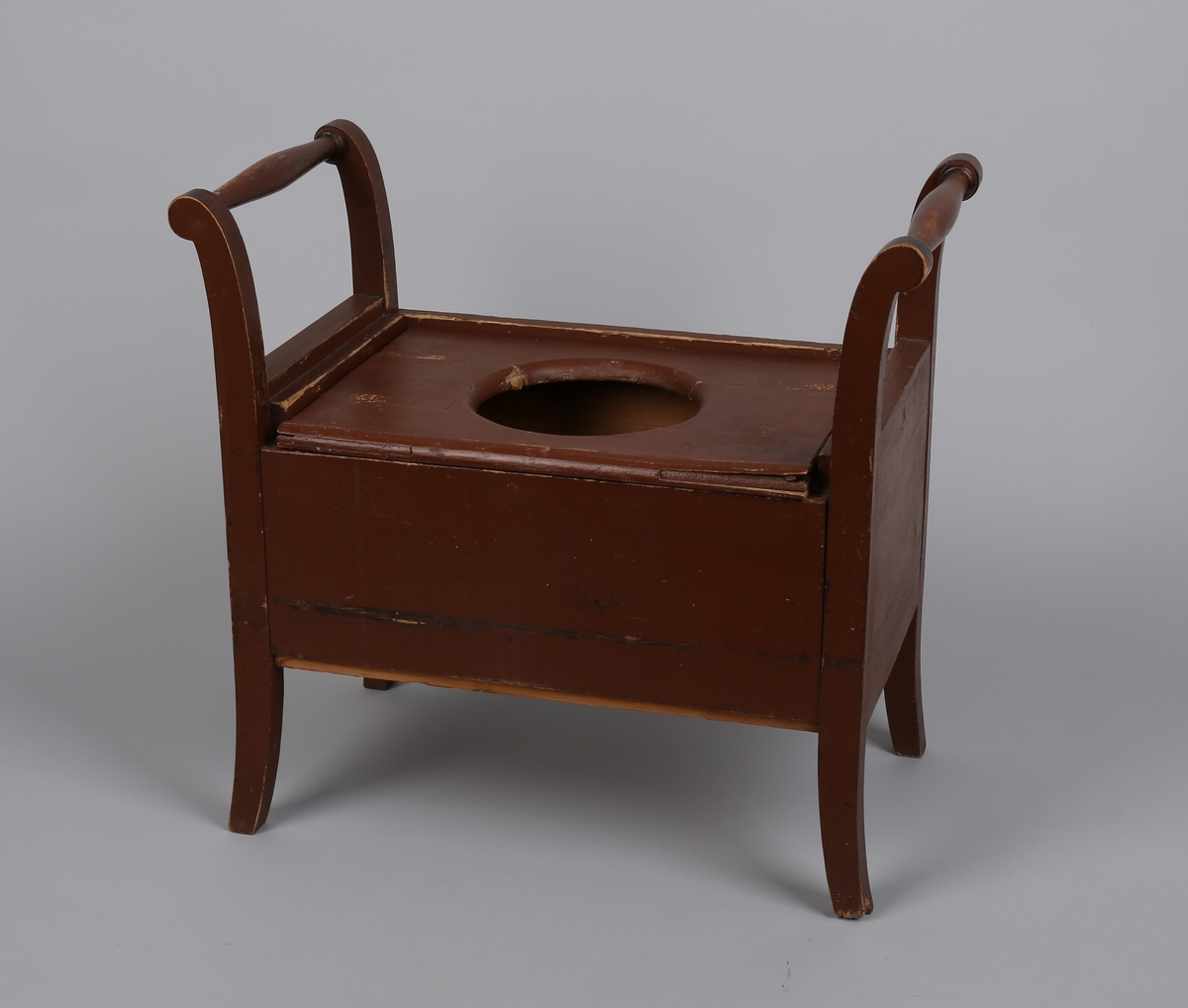 Rektangulær stol uten ryggstø (krakk). Dreide, utoverbøyde håndtak på sidene. Lokk med hull til potte/dobøtte.