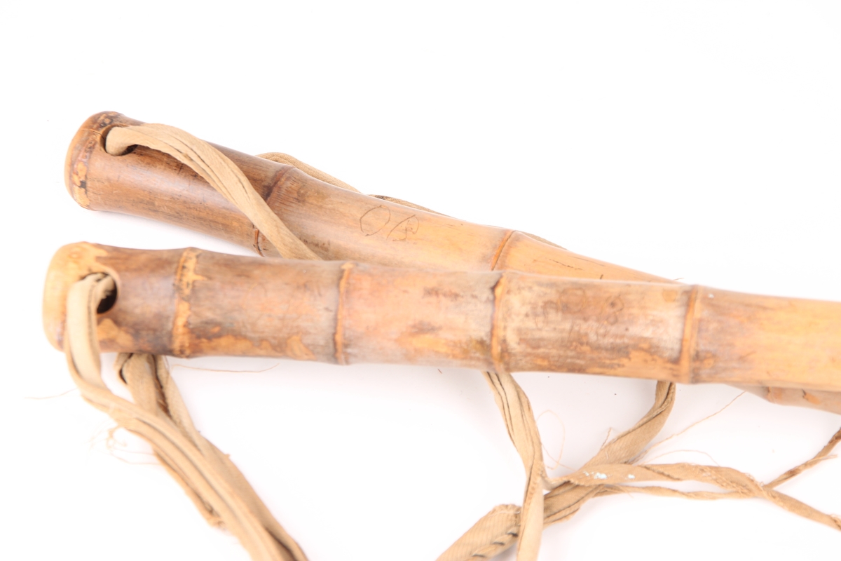 Et par bambusstaver med håndtaksremmer i bomull, samt mørke horn(?)-trinser. Trinsen er festet til staven med en lærrem, som går gjennom et hull i staven. Nederst på staven er det festet en holk og stavpigg i jern.
Det er surret tråd rundt den nederste delen av stavene, trolig i forbindelse med en reparasjon da begge stavene er sprukket.