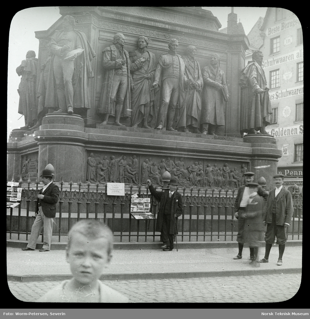 En gutt i forgrunnen og noen menn står foran et monument av Friedrich Wilhelm III i Køln.