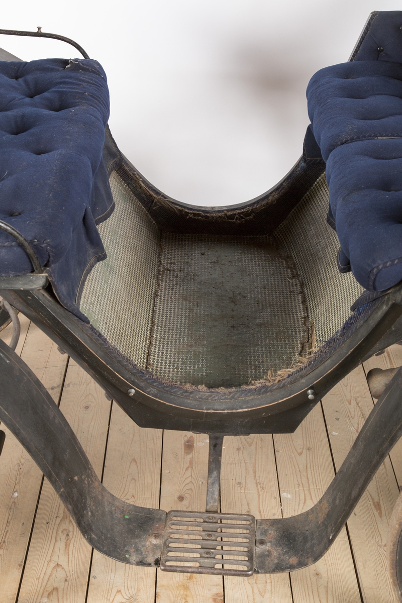 Bak- sete, motsete og kuskesete er trukket med blått stoff og kantet m/blått ullbånd. Setene er polstret. Baksetet har knapper i rygg og på setet.  Over fatingen er det festet et lær- trekk som er fòret m/blått ullstoff.