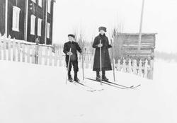 Gutt og jente med ski foran stort bolighus
