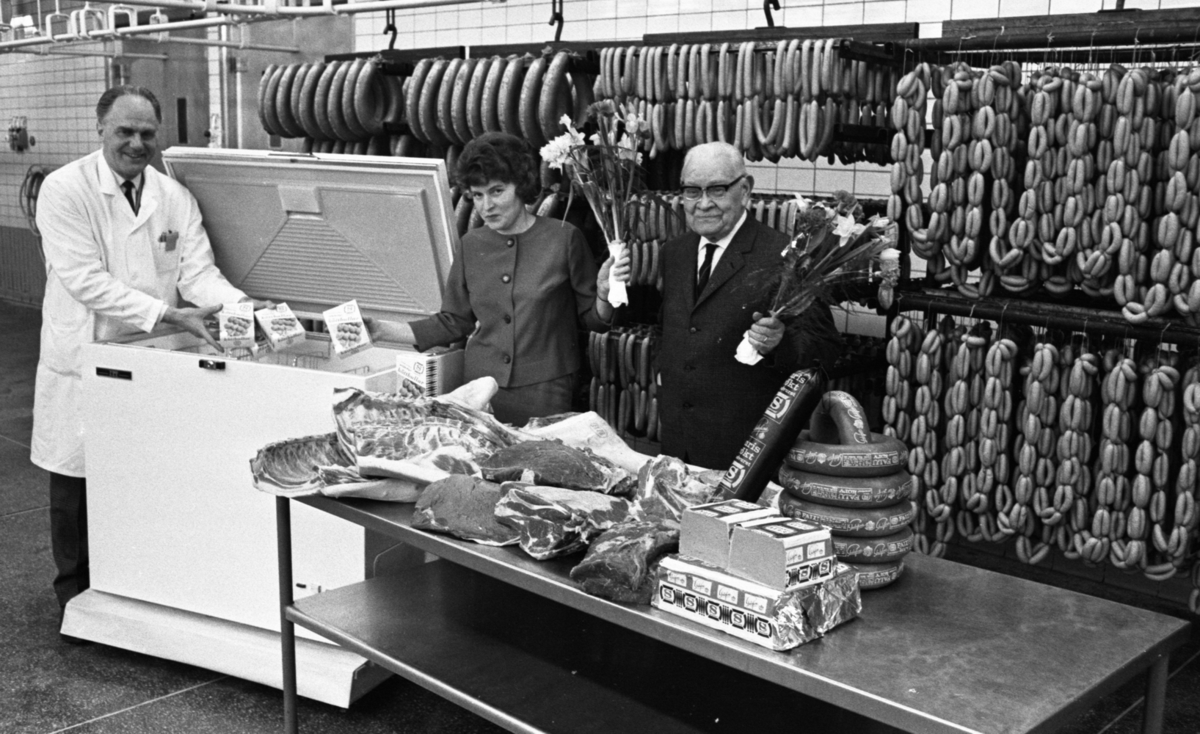 Orubricerat 18 februari 1966

I en charkuterifabrik står två män och en kvinna. Den äldre herrn till höger på bilden håller en bukett blommor i handen. Frysboxen flankeras av en man och en kvinna. Mannen håller i två stycken paket  med påskriften "Köttbullar" samt ett märke med bokstaven "S." I sin högra hand håller hon ett sådant köttbullspaket och i den vänstra håller hon en blombukett. Framför sällskapet finns ett bord med leverpastej, korvar samt fläskkött. Leverpastejen samt korvarna har bokstaven "S" på förpackningarna.  Bakom dem hänger korvar i  tre olika storlekar.