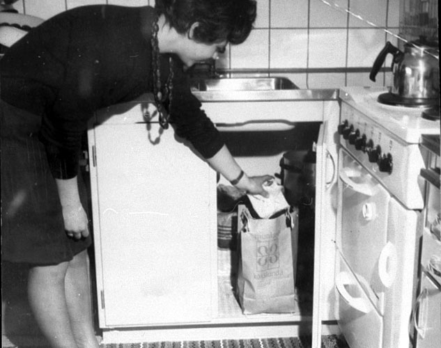 Kvinlig hyresgäst visar det moderna kökets sophantering i Rostaområdet på 1950-talet.
