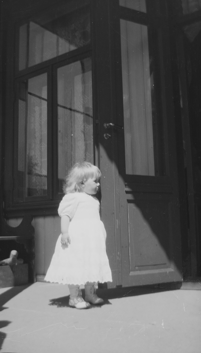 En liten Iacob Ihlen Mathiesen står på en veranda og kikker inn gjennom en åpen dør.