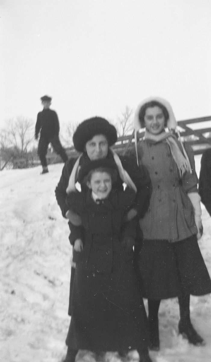 I front har står tre personer, en jente og to kvinner, bak dem står en ung gutt. De er kledd for vinter og står i en snødekket skråning.