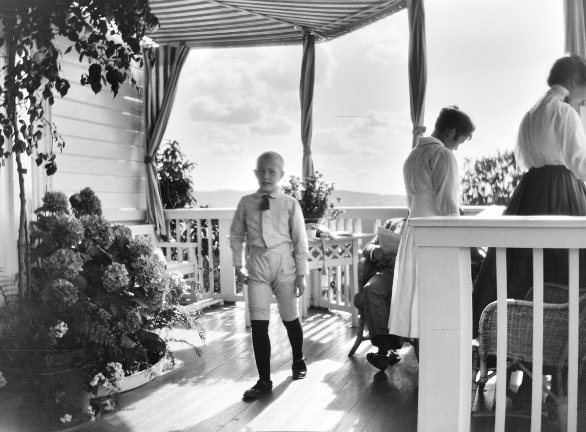 Fire personer oppholder seg på den halvsirkelformede verandaen som vender mot den viktorianske hagen på  Linderud Gård. Iacob Ihlen Mathiesen går mot fotografen.