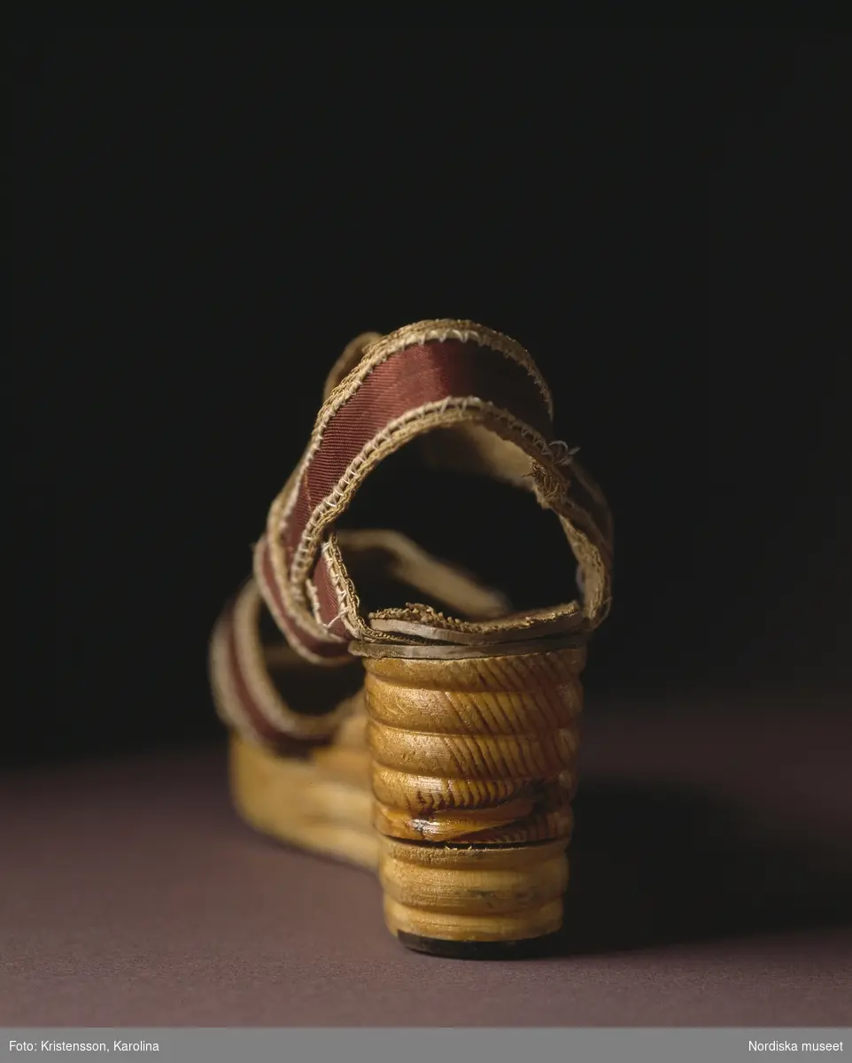 Sandalett, så kallad surrogatsko, med band av papper och konstsilke. Den kraftiga kilklacken är av trä. Föreskrifterna var många under krigsårens råvaruransonering.