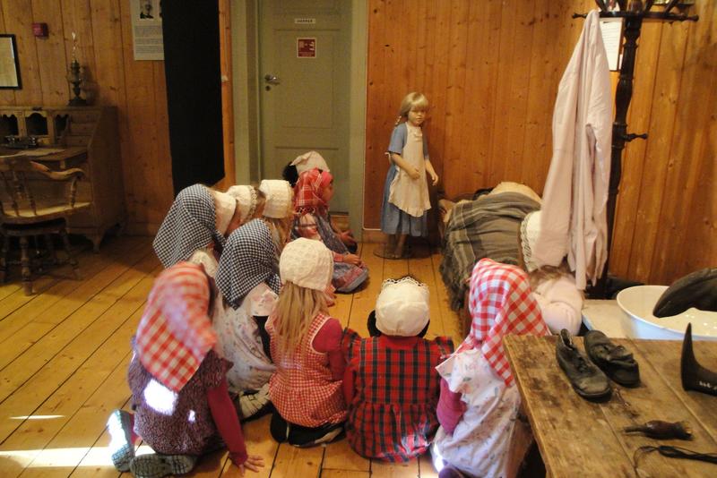 Barn sitter på gulvet i gammeldagse kostymer og lytter til historien om lille Maren og Skinnfell-Marja.