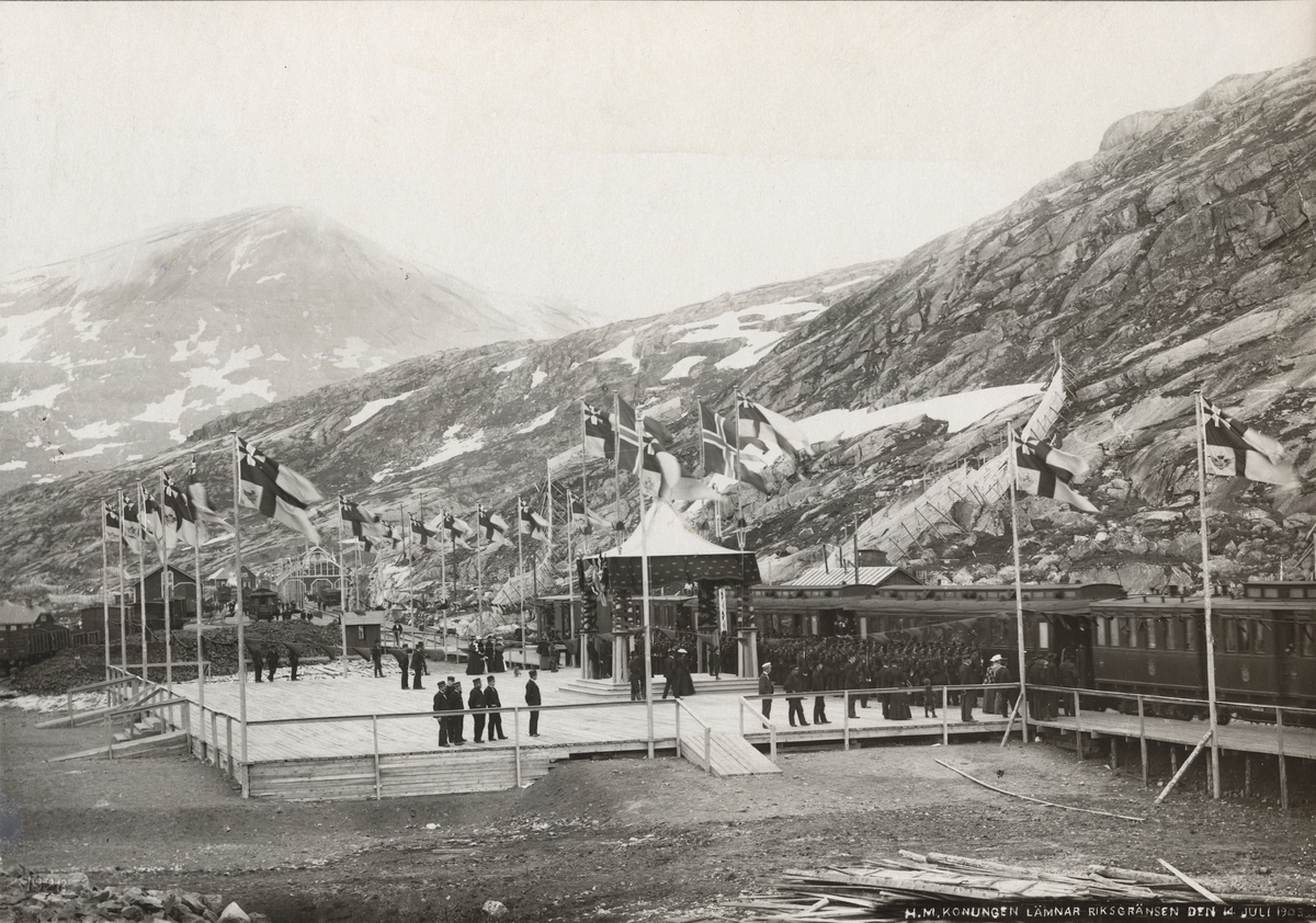 Från Riksgränsbanans byggnation: Riksgränsens station, dekorerad med svenska och norska flaggorna i topp vid invigningen den 14 juli 1903. Invigningståget med kung Oscar lämnar stationen för att fortsätta till Narvik.