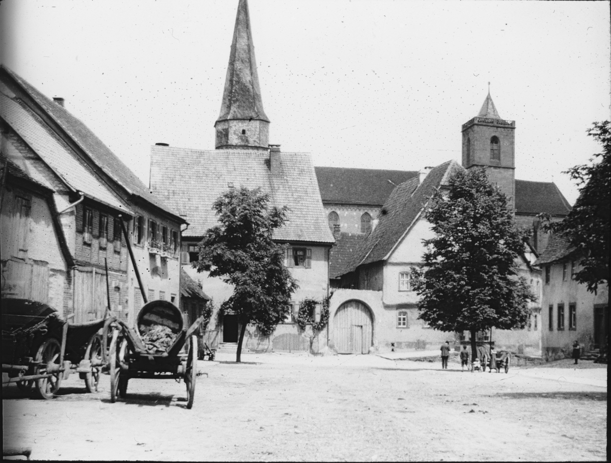 Skioptikonbild med motiv från Anger i Münnerstadt med Stadtpfarrkirche St. Maria Magdalena i bakgrunden.
Bilden har förvarats i kartong märkt: Vårresan 1910. Münnerstadt.