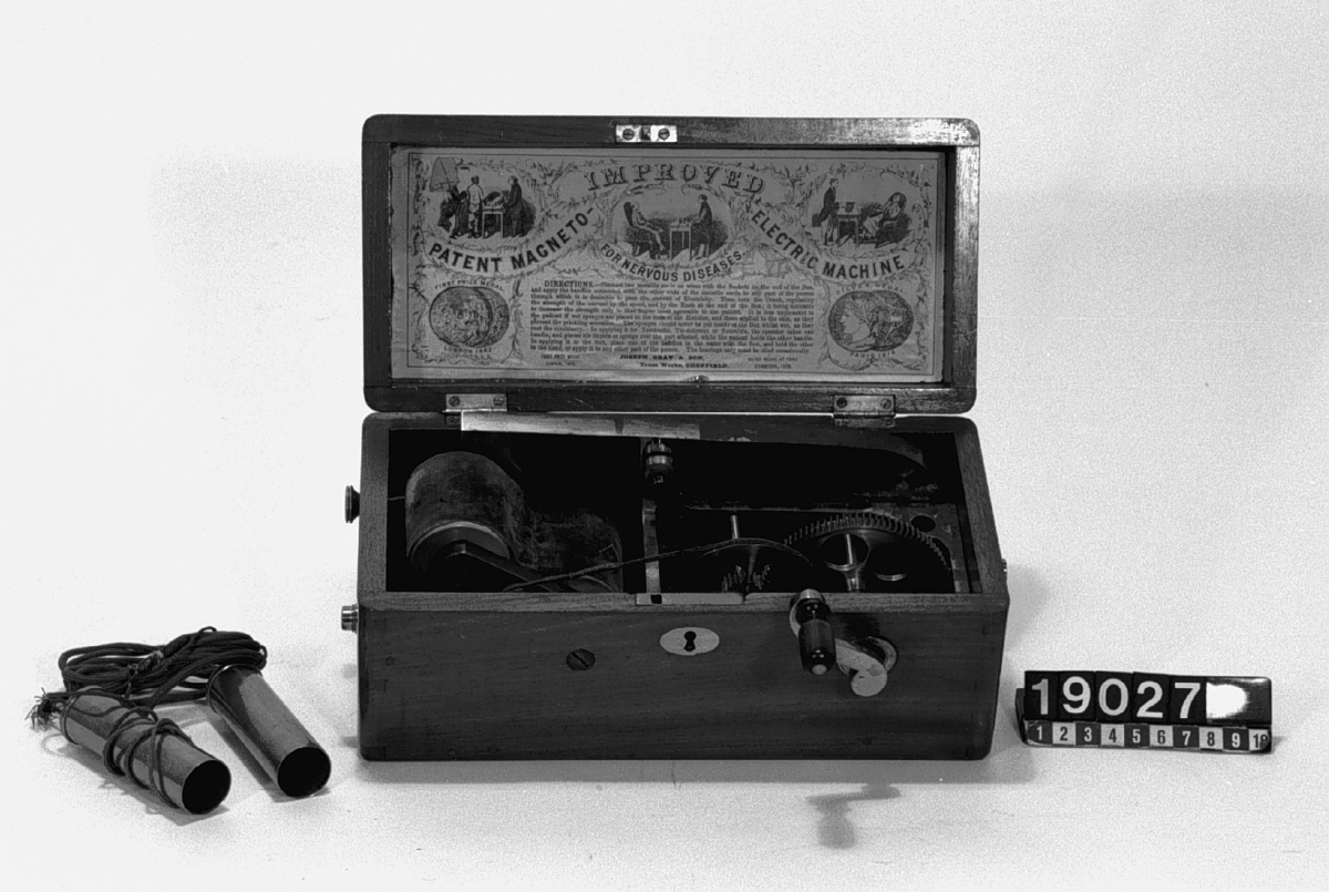 Apparat i låda av trä, etikett med bruksanvisning i locket, två handtag av mässing med ledningar, nyckel till lås och vev.