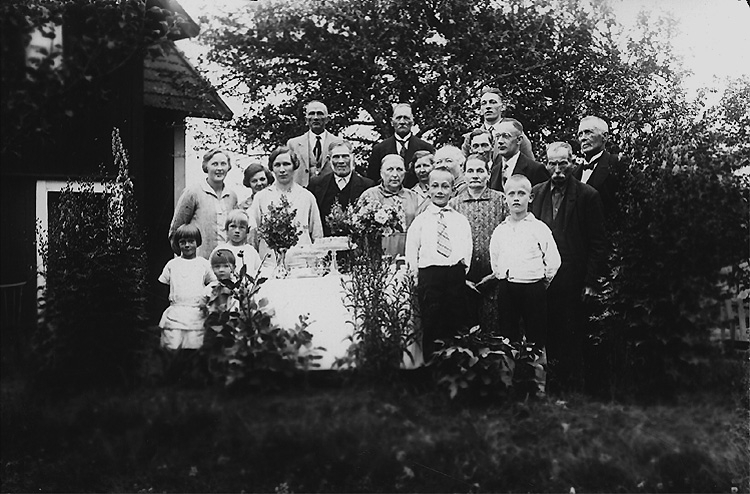 Gruppbild 20 personer i trädgården.
Bostadshus.
Familjen Gustafsson i Lövsätter med besökare från Norrbyås, bl.a. lärare Elander, Fridhem, till höger, med fler.