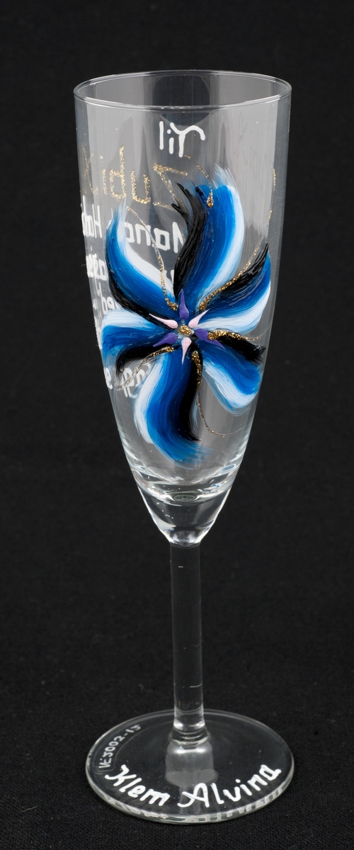 Høyt stetteglass med påskrift og dekor i blått, svart og hvitt; med innslag av rosa, fiolett og gull.