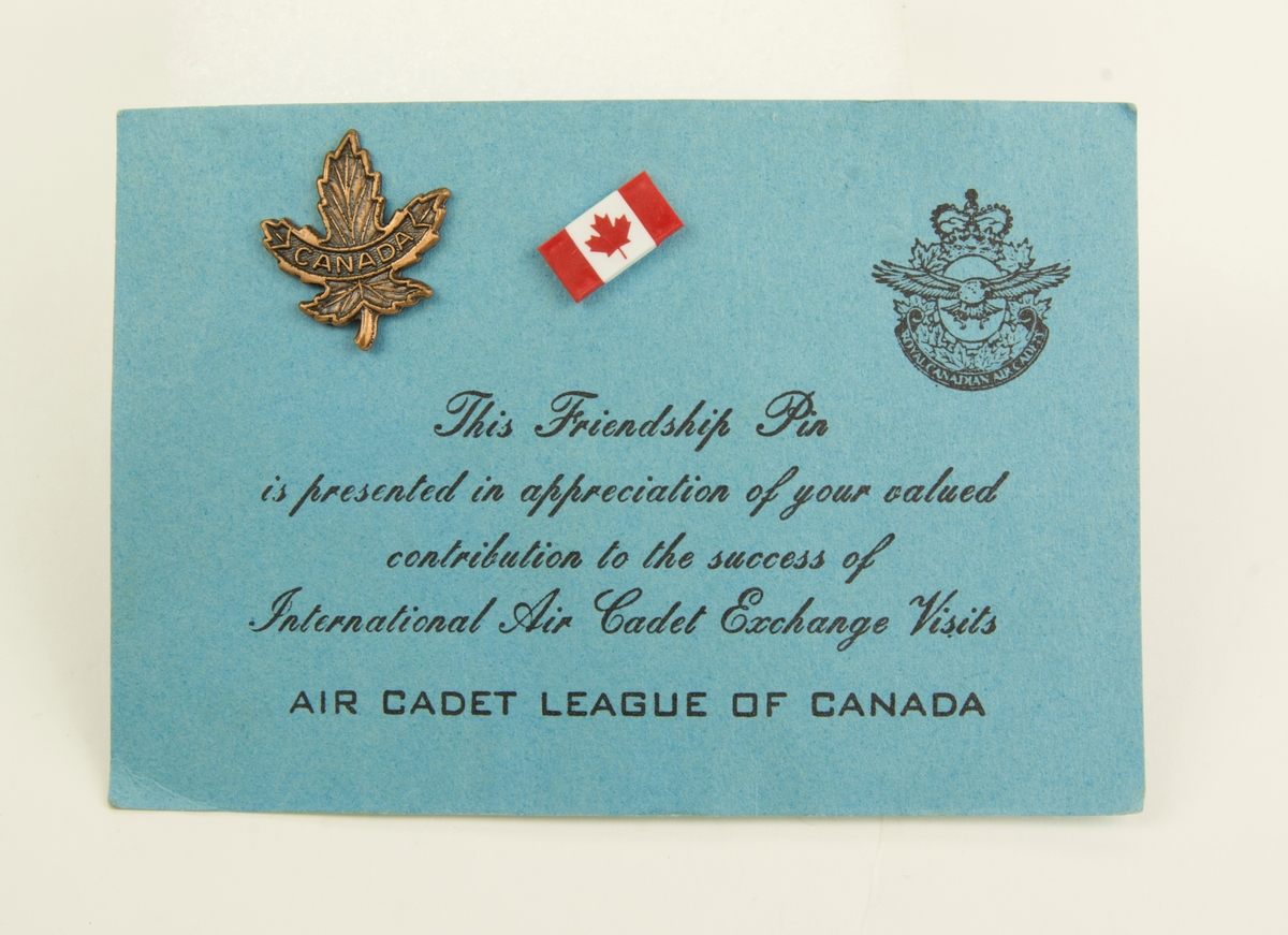 Två nålar till rockslag. Nål 1 är bronsfärgad med formen av ett lönnlöv med texten: CANADA Nål 2 är Kanadensiska flaggan. Nålarna är fästa på ett tillhörande pappersark.