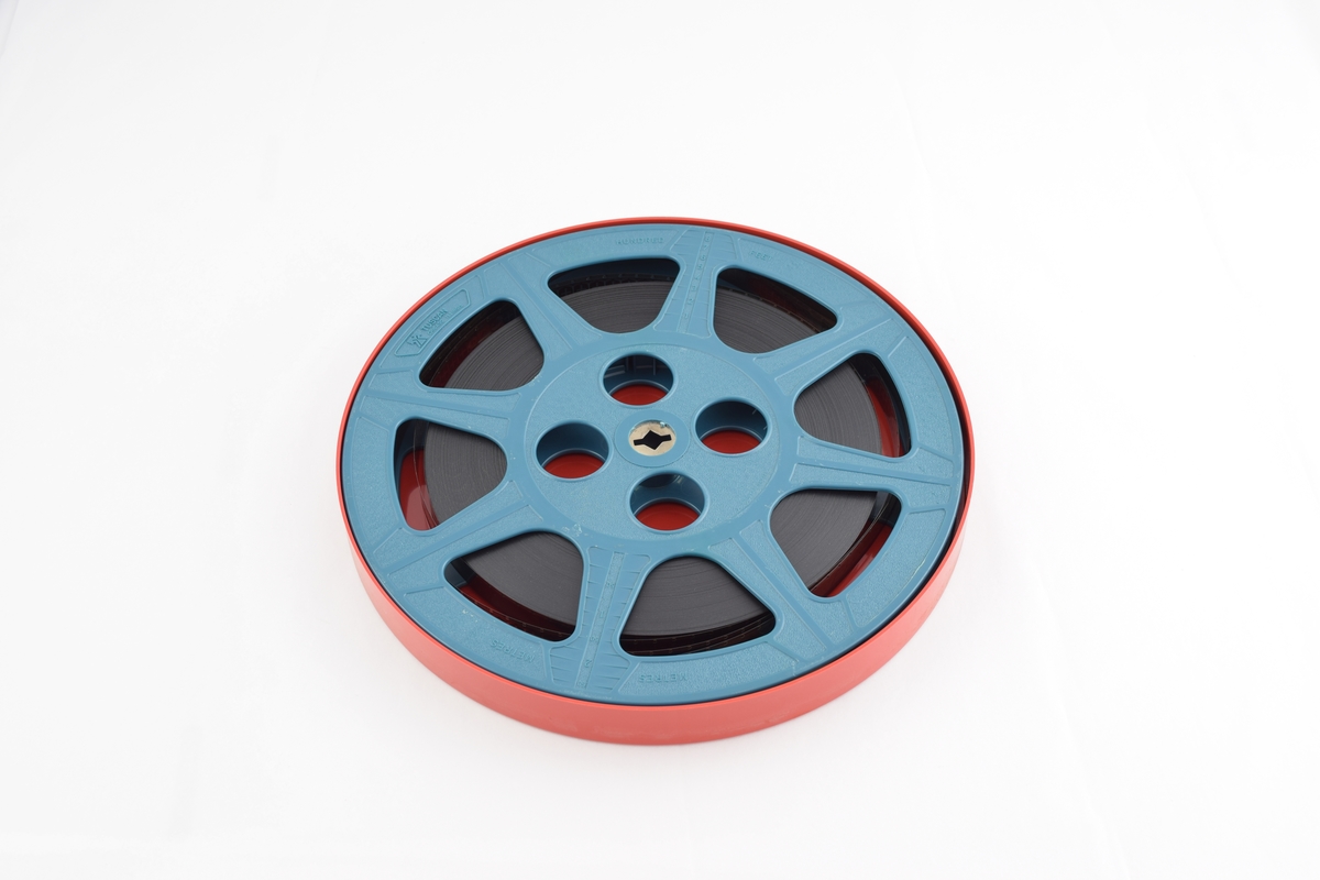 Filmrull i eske. Film på blå plastikkspole. Rødt rundt etui med rund grønn etikett.