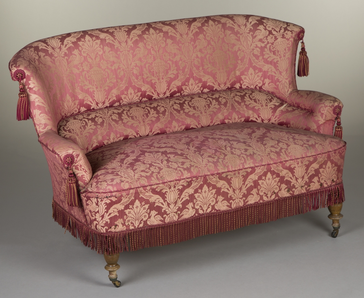 Det symmetriske og gjentakende motivet på stoffet til sofaen er preget av bladverk, blomster, fugler og urner.